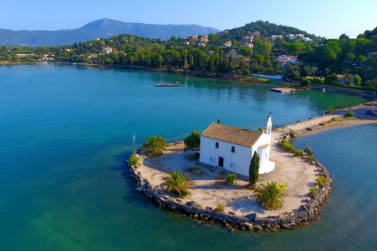 Whitewashed Ypapanti Church on a small islet off a calm, sheltered Corfu cove